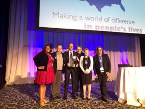 Image of six individuals at Annual Conference. One person is holding an awards. 