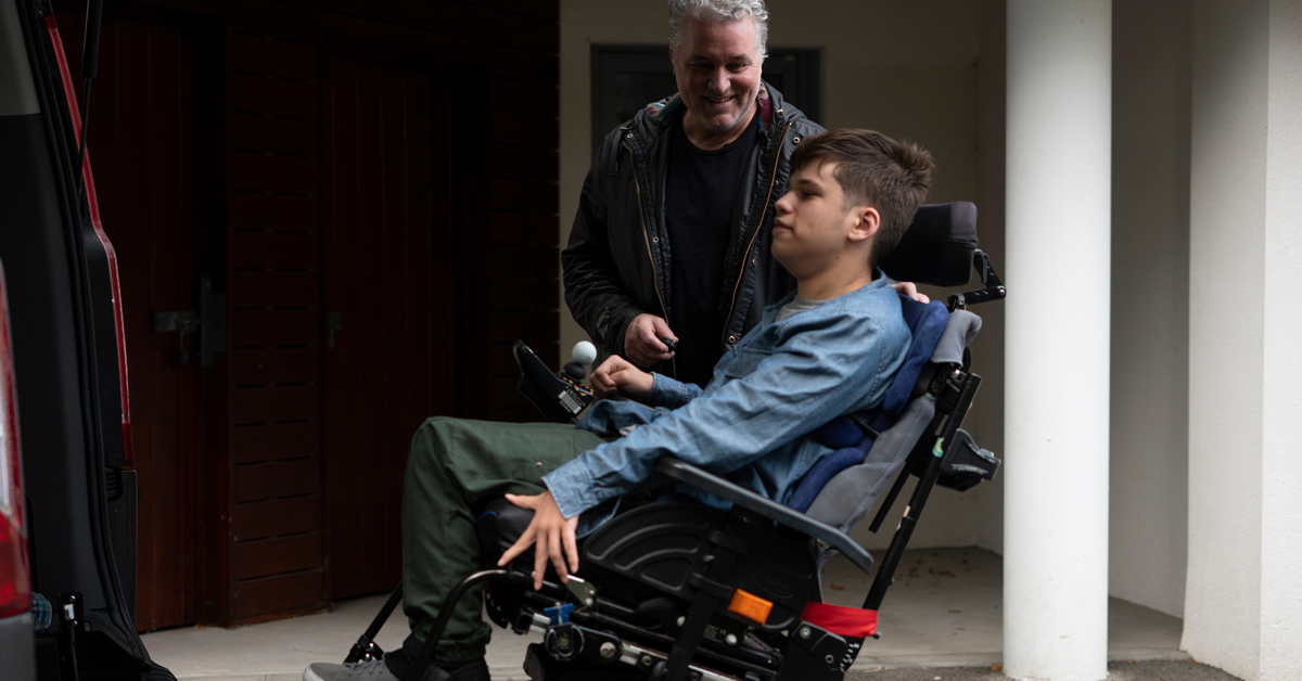 An middle-aged man helps support a person using a wheelchair transfer into an accessible van.